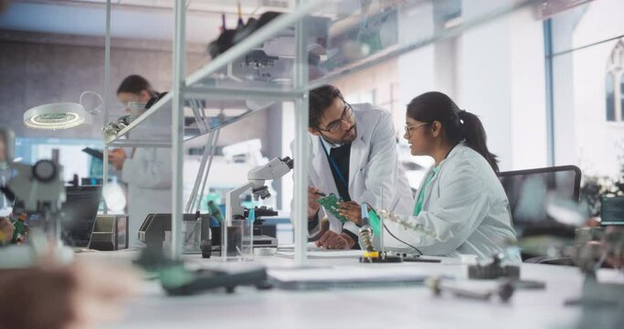 Two Diverse Multiethnic Colleagues Chatting in Laboratory, Working on a Circuit Board for a Computer. Young Indian Scholar Talking with a Scientist About Inserting Different Microchips and Conductors