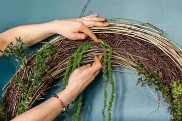 Fototapeta na wymiar Woman makes home decor from natural materials,hands close-up.The process of making a wreath of twigs,stabilized moss.and leaves.Biophilia design concept.