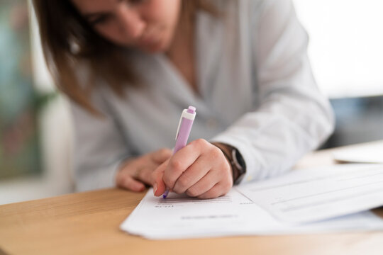 High angle of crop anonymous female in casual clothes sitting at wooden table checking printed expenses bill next to a computer