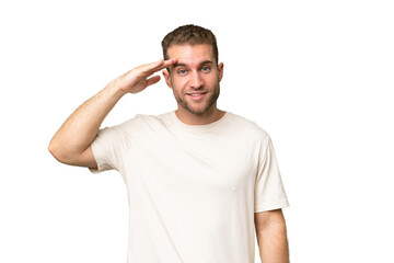 Young handsome caucasian man isolated on green chroma background saluting with hand with happy expression