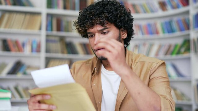 Close up Sad university student reading letter with bad news sitting in campus library space. Disappointed applicant holds an envelope with an unpleasant notification about unsuccessful entrance exams