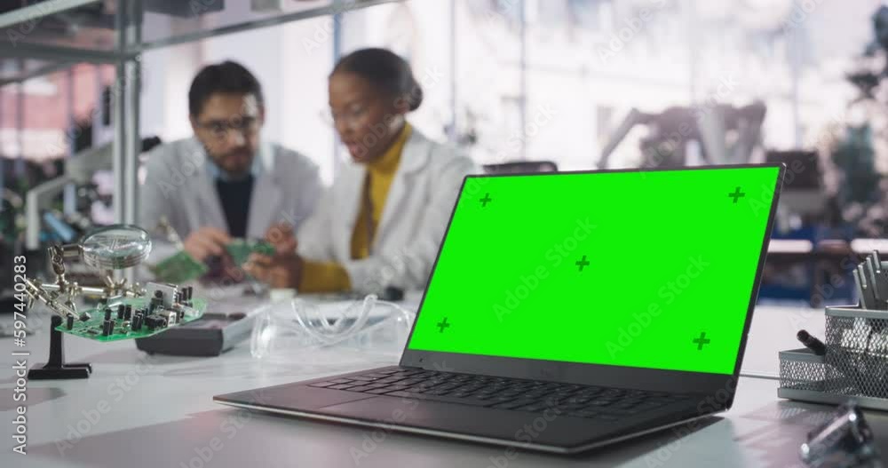 Aufkleber Laptop Computer with Green Screen Mock Up Display Standing on a Table in a Science Class Laboratory. Diverse University Graduates Having a Conversation About Their Electronics Project