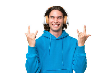 Young handsome man isolated on green chroma background listening music making rock gesture