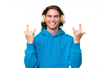 Young handsome man isolated on green chroma background listening music making rock gesture