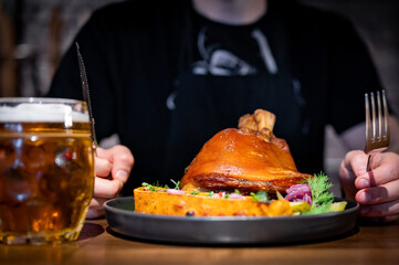 man cuts a pork knuckle with a knife and fork