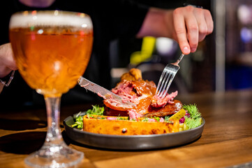 man cuts a pork knuckle with a knife and fork