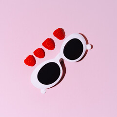 White round glasses on a pink background among raspberries in a minimalist style. Flat lay, top view.