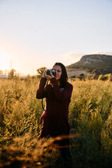 A young woman strolling through the countryside with her vintage camera at sunset.