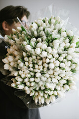 Very nice young man holding big and beautiful bunch of fresh blossoming white tulip flowers, close up view   - 597444041