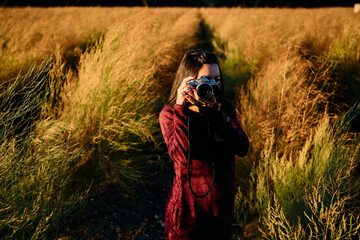 A young woman strolling through the countryside with her vintage camera at sunset.