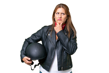 Middle-aged caucasian woman with a motorcycle helmet over isolated background having doubts