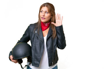Middle-aged caucasian woman with a motorcycle helmet over isolated background listening to something by putting hand on the ear