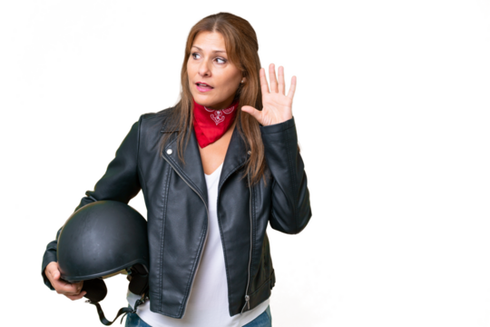 Middle-aged caucasian woman with a motorcycle helmet over isolated background listening to something by putting hand on the ear