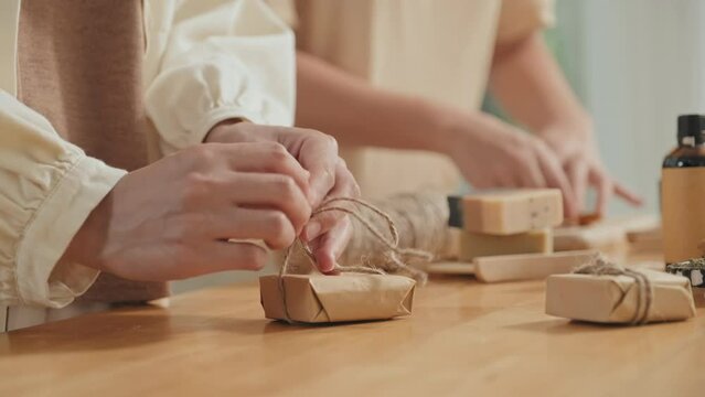 Cropped shot of unrecognizable women wrapping handmade soap in craft paper
