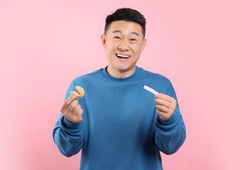 Happy asian man holding tasty fortune cookie with prediction on pink background