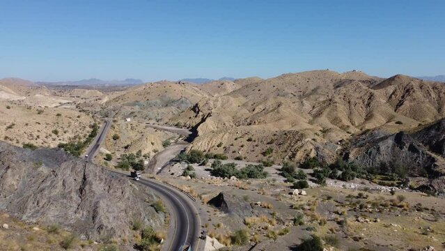 Aerial drone forward moving shot over cars and trucks moving on a winding RCD road through Balochistan on a sunny day.