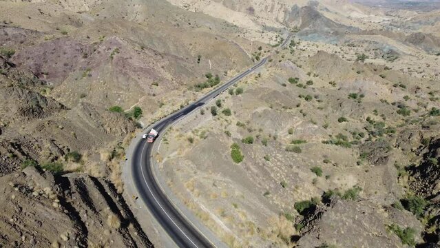 Aerial drone forward moving shot over cars and trucks moving on a winding RCD road through Balochistan on a sunny day.
