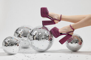 Woman in pink high heeled shoes and disco balls on white background, closeup