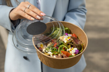 A woman is holding a container of salad.