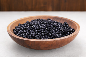 Fototapeta na wymiar Bowl of raw black beans on light grey table, closeup