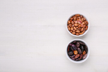 Bowls with different types of beans on white wooden table, flat lay. Space for text