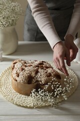 Woman decorating delicious Italian Easter dove cake (traditional Colomba di Pasqua) with flowers at white wooden table, closeup