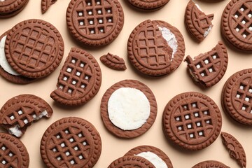 Tasty chocolate sandwich cookies with cream on beige background, flat lay