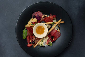 A glass of white wine sits on a table with a platter of meat cheese