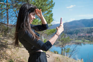 Beautiful woman standing above lake making selfie pictures with her mobile phone . 