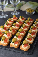 Festive canapes with red caviar and olives on croutons of white bread on slate board on gray background, Closeup