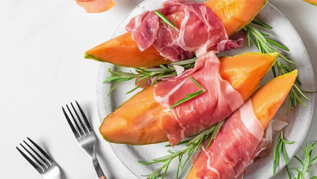 Italian antipasti. Melon cantaloupe slices with prosciutto ham, rosemary and honey in a plate on white background. top view. Healthy food