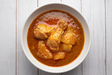Chicken massaman with potato in white bowl on wooden table.
