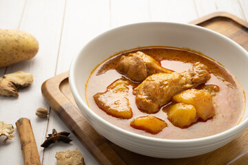 Chicken massaman with potato in white bowl on wooden table.