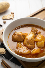 Chicken massaman with potato in white bowl on wooden table.