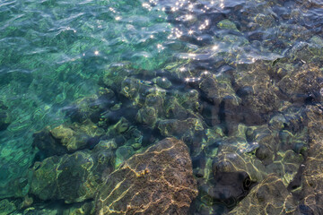 Gleaming aquamarine sea water with shiny sparkles and rocks underwater