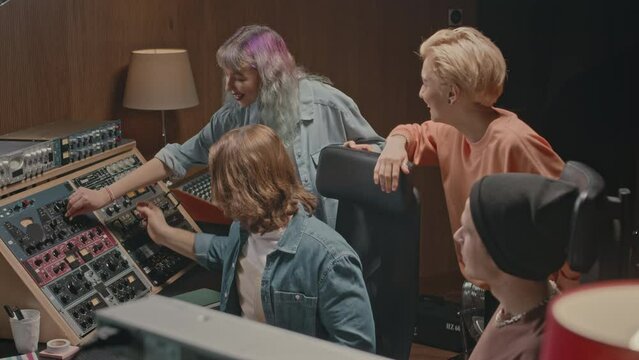 Members of modern music band and their producer using mixing console while coworking on new album together at recording studio
