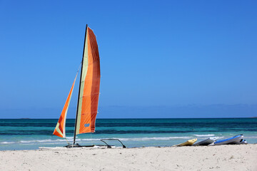 Catamaran sailboat on a sand on blue sea background. Water sports on summer beach