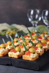 Canapes with red caviar and olives on croutons of white bread on dark board on gray background