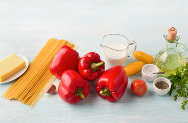 Ingredients for pasta with vegetables: spaghetti, sweet red peppers, tomatoes, cream, cheese, garlic, olive oil, parsley and spices on a blue background