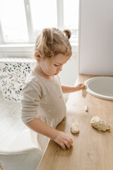 Fototapeta premium Little kid daughter having fun cooking pastries or pie on kitchen table top. Child knead dough, cooks pizza, bake cookies, dumplings, croissants for mother, father. Family preparation food on weekend.