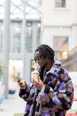 young man Afro using his phone and drinking a coffee