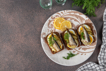 Homemade hot sandwiches with sprats, egg, cheese and pickled cucumber on plate on brown background