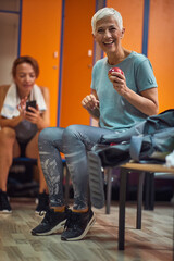 Mature senior woman in sportswear sitting on bench in gym locker room.