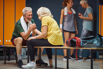 Senior man and woman arm wrestling and having fun in gym locker room.