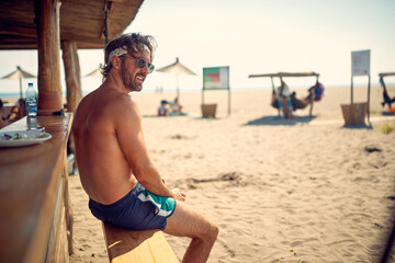 A young guy is sitting in the bar on the beach and enjoys the view. Summer, beach, sea
