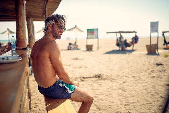 A young guy is sitting in the bar on the beach and enjoys the view. Summer, beach, sea - Powered by Adobe