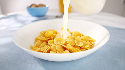 corn flakes in a bowl. milk is poured into a bowl of cereal. healthy breakfast on the table on a sunny day.