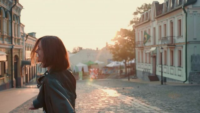 Beautiful and happy woman runs through town in beautiful dawn light, turns to camera, spinning and smiling