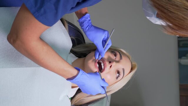 a female dentist examines patient's teeth in dental clinic. Doctor probes teeth with dental instrument with guide, looks for treatment for caries and checks for problems with filling. vertical video