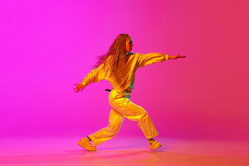 Fototapeta na wymiar Portrait with one young attractive woman, dancer with pigtails dancing over gradient pink background in neon light. Side view. Contemporary dance style